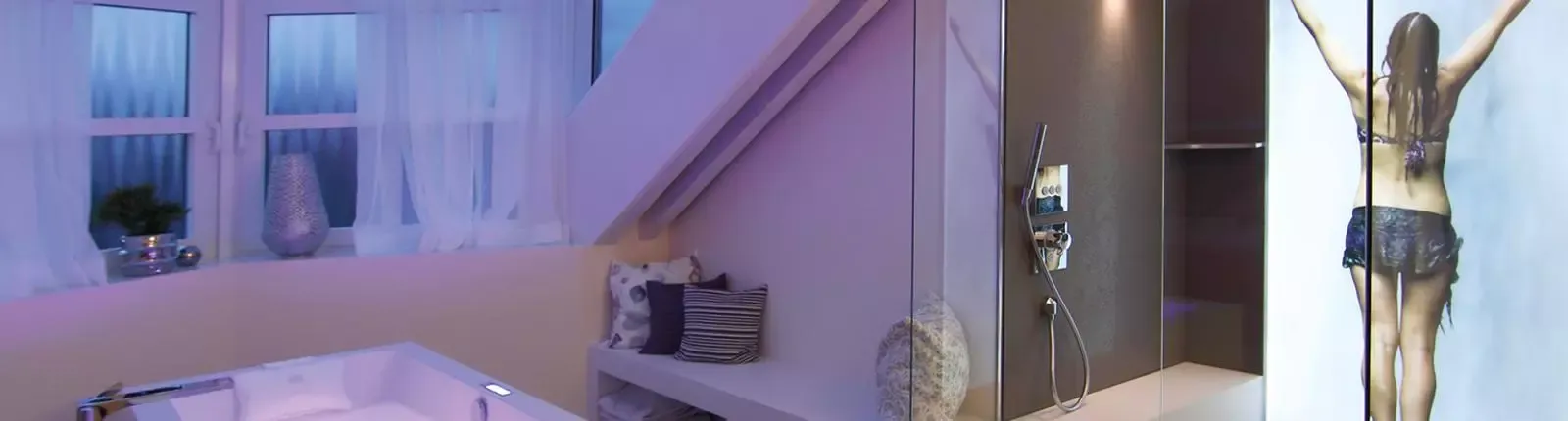 Luxuriöses Badezimmer im Obergeschoss mit Badewanne, Glasdusche und atmosphärischer LED-Beleuchtung in Violett und Blau.