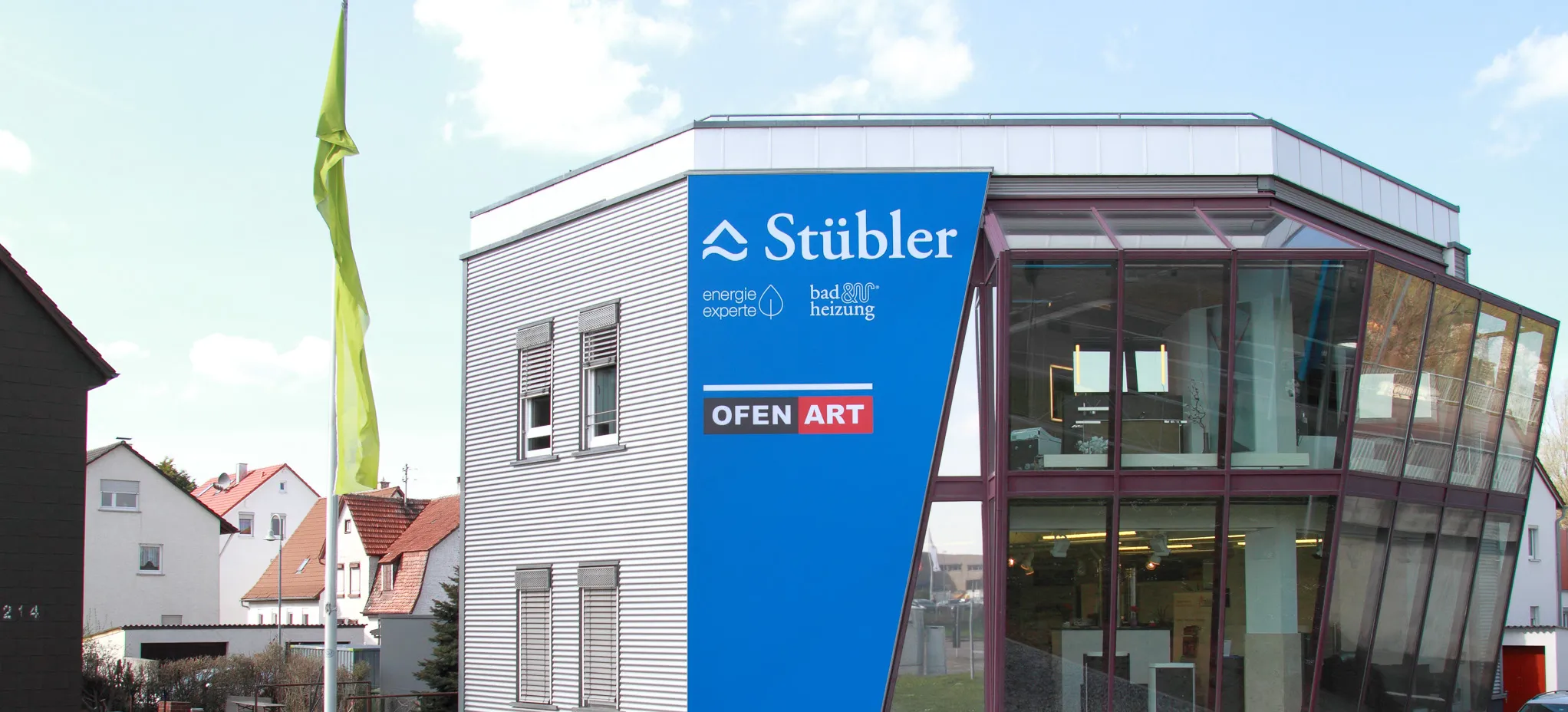 Modernes Firmengebäude der Stübler GmbH mit markanter Glasfassade und blauer Außenbeschriftung, gelegen in einem Wohngebiet mit angrenzender Grünfläche.