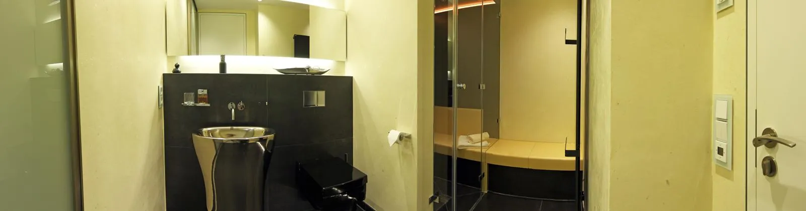 Modernes Gästebad mit freistehendem Edelstahl-Waschtisch, großem Spiegel und angrenzender Dampfsauna mit Glasfront und Sitzbank.