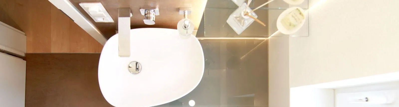 Modernes Gäste-WC mit weißem Aufsatzwaschbecken, Wandarmatur und dekorativen Accessoires auf Glasablage, fotografiert aus der Vogelperspektive.