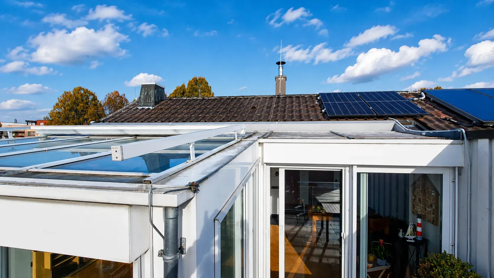 Modernes Wohngebäude mit Dach-Photovoltaikanlage, Glasanbau und energieeffizienter Bauweise. Die Kombination aus Solarmodulen und lichtdurchflutetem Wintergarten verbindet nachhaltige Energietechnik mit modernem Wohnen.