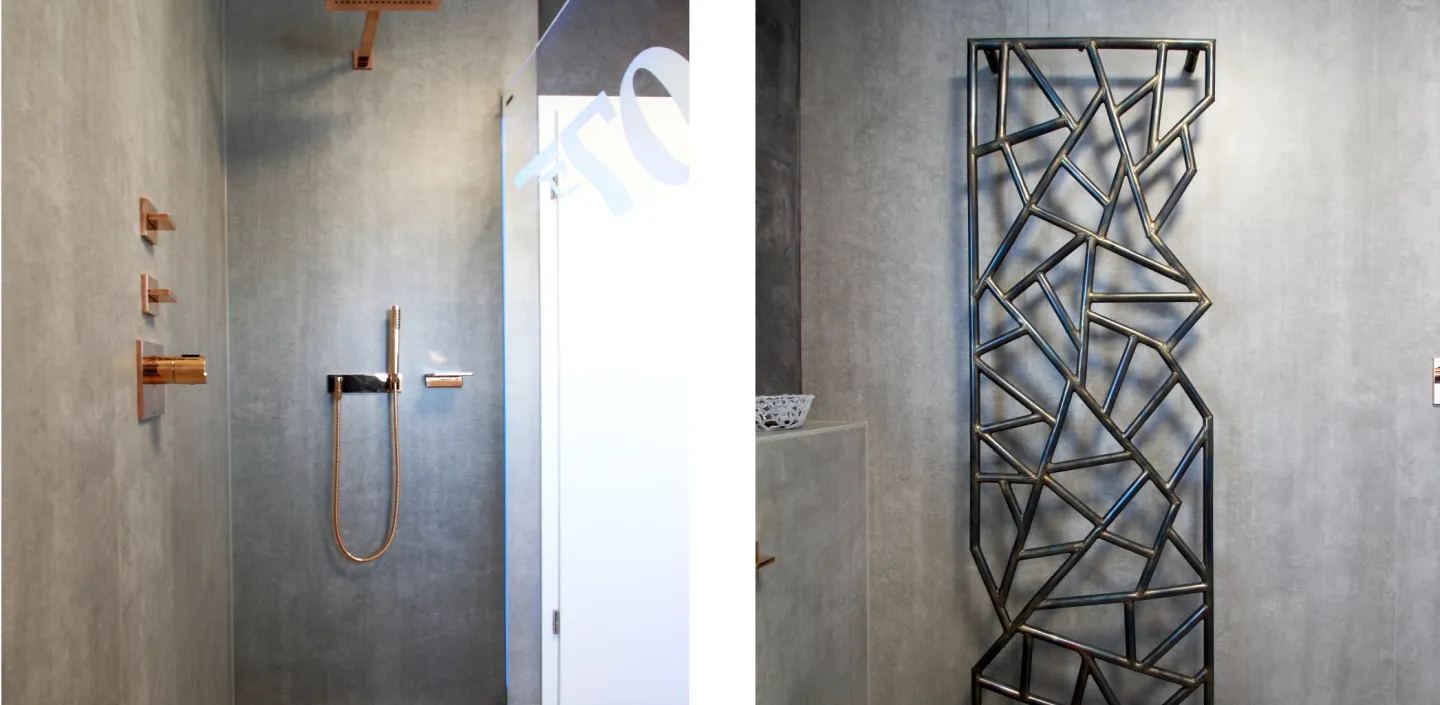 Wohnbad in Straßdorf mit bodenebener Dusche und goldfarbenen Armaturen links sowie modernem geometrischem Designheizkörper an grauer Wand rechts.