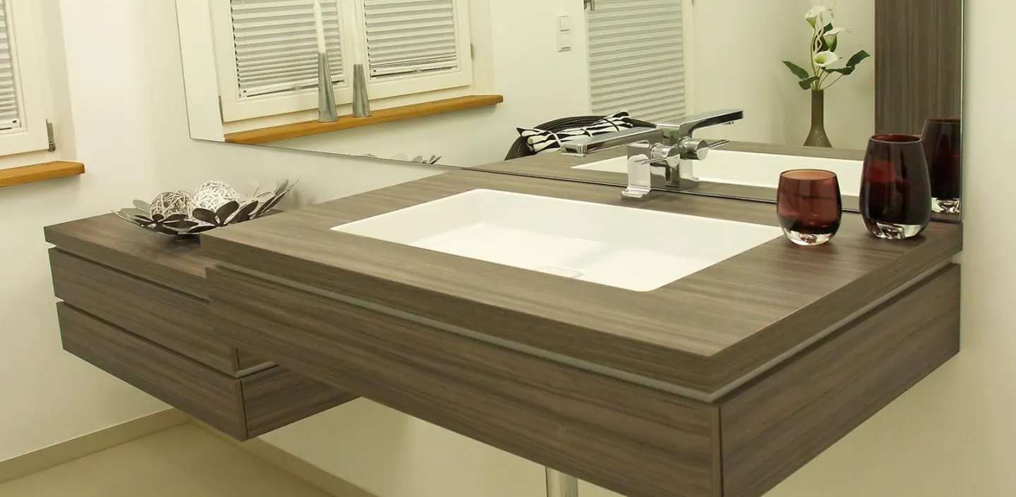 Moderner Waschtisch aus Holzoptik mit weißem Waschbecken, Spiegelwand und stilvoller Dekoration.
