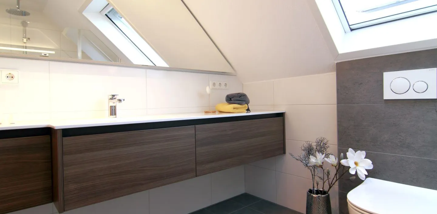 Helles, modernes Dachbad mit großem Waschtisch, wandhängendem WC, Dachfenster und dekorativer Vase mit Blumen.