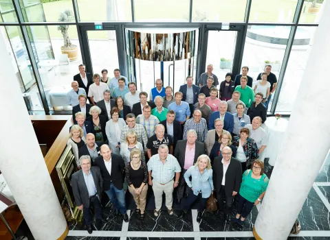Eine große Gruppe von Menschen posiert in einem modernen Gebäude mit einer Glasfassade für ein Gruppenfoto.