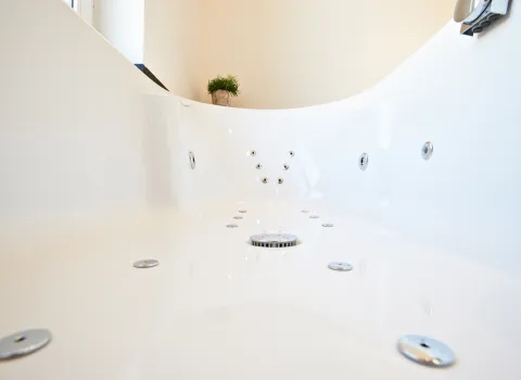 Nahaufnahme des Innenraums einer modernen Whirlpool-Badewanne mit mehreren eingelassenen Düsen und einem runden Abfluss in der Mitte. 