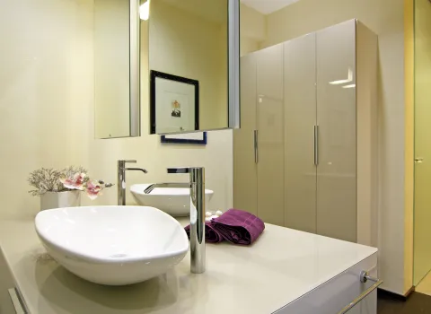Modernes Badezimmer mit schwebendem Waschtisch, zwei eleganten Aufsatzwaschbecken, großem Spiegelschrank, Hochglanzschränken und dekorativen Akzenten.
