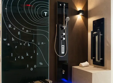 Design-Duschkabine im Showroom der Stübler GmbH mit schwarzer Duschsäule, stilvollem Sitzbereich, indirekter LED-Beleuchtung und künstlerisch bedruckter Glaswand mit Wettergrafik.