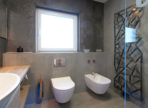 Wohnbad in Straßdorf mit wandhängendem WC, Bidet, moderner Steinoptik-Verkleidung, Holzablage und Designheizkörper in geometrischer Form.