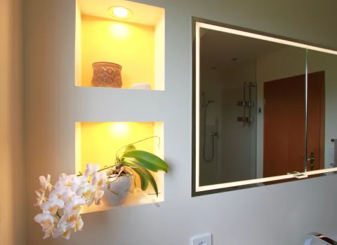 Beleuchtete Wandnische mit weißer Orchidee und Dekoelementen neben einem modernen Spiegelschrank im Badezimmer.