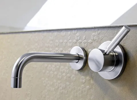Moderne, silberne Wandarmatur mit Hebelgriff in einem eleganten Dachbad, montiert vor strukturierter Wandverkleidung.