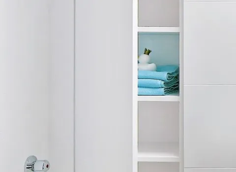 Weißer Einbauschrank im Dachbad mit geöffneter Tür, Regalfächern und ordentlich gefalteten Handtüchern.