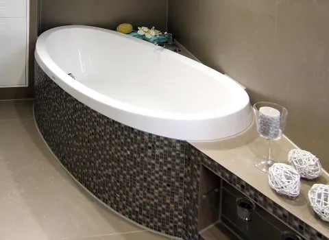 Elegante Badewanne mit dunklen Mosaikfliesen und dekorativen Accessoires in einem modernen Dampfbad.