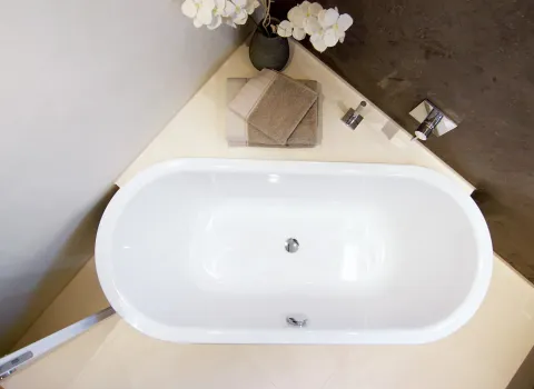 Weiße Badewanne in Vogelperspektive mit grauen Handtüchern und Orchideen-Dekoration vor einer Steinwand im modernen Badezimmer.