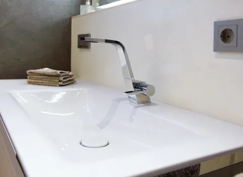 Modernes Waschbecken mit glänzender Chromarmatur, hellen Fliesen und neatly gefalteten Handtüchern auf dem Waschtisch.