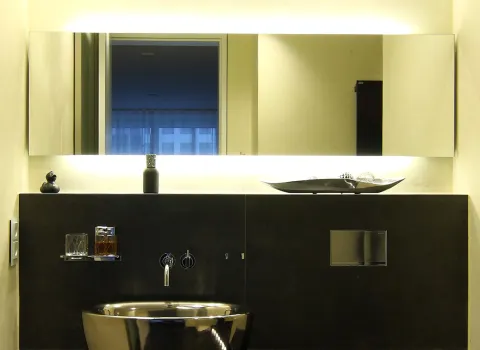 Moderner Waschtisch mit beleuchtetem Spiegel, schwarzen Wandfliesen und eleganten Accessoires in einem Gästebad mit Dampfsauna.