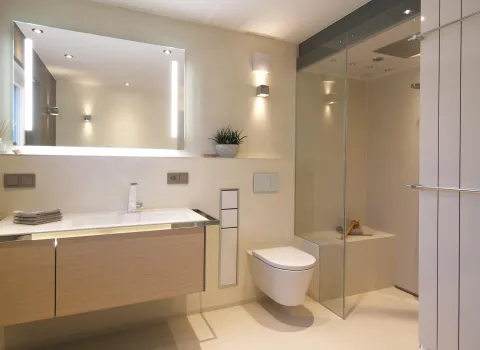 Modernes Badezimmer mit großem beleuchtetem Spiegel, hellem Holzwaschtisch, wandhängendem WC und bodengleicher Glasdusche im minimalistischen Design.