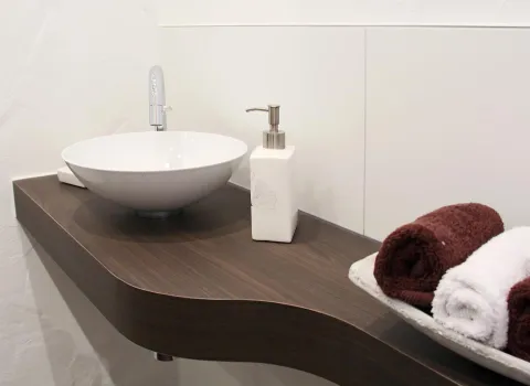 Modernes Gästebad mit rundem Aufsatzwaschbecken auf dunkler Holzablage, Seifenspender und dekorativ gerollten Handtüchern.