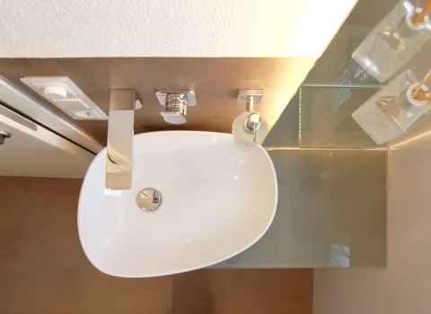 Stübler Gäste-WC mit modernem Aufsatzwaschbecken, eleganter Wandarmatur und dekorativen Glas-Accessoires, aus der Vogelperspektive fotografiert.