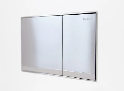 Moderne, rechteckige Betätigungsplatte von Geberit in Edelstahloptik mit zwei Spültasten, eingebaut in eine weiße Badezimmerwand.