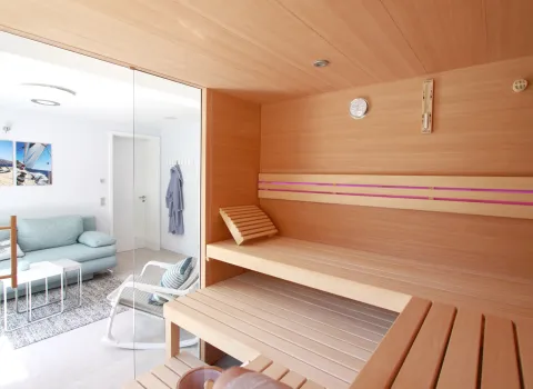 Blick aus der modernen Privatsauna mit Glasfront in den Wellnessbereich mit Sofa und Relaxstuhl.