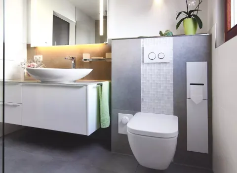 Modernes barrierefreies Badezimmer mit weißem Aufsatzwaschbecken, Wand-WC, beleuchtetem Spiegel und grauen Fliesen.