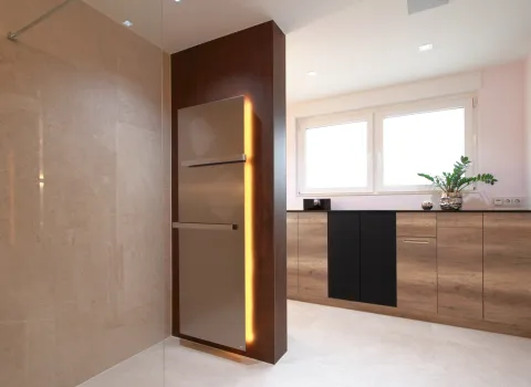 Modernes Wohnbad mit Designheizkörper in Edelstahloptik mit integrierter Beleuchtung, großen Natursteinfliesen und maßgefertigten Holzschränken unter dem Fenster.