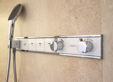 Moderne Duscharmatur von Hansgrohe mit Temperaturregelung und Bedienknöpfen, montiert an einer Wand aus hellen Natursteinfliesen.