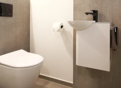 Kompaktes Gäste-WC mit wandhängender Toilette, schwarzer Betätigungsplatte, kleinem weißen Waschbecken mit schwarzer Armatur und seitlichem Handtuchhalter.
