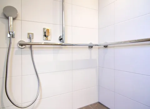 Barrierefreie Dusche im altersgerechten Dachbad mit Handbrause, moderner Armatur und stabilem Haltegriff.
