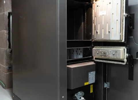 Moderne Pelletheizung mit geöffneter Brennkammer in einem technischen Heizraum. Die schwarze Heizungsanlage zeigt den Innenbereich des Pelletkessels mit geöffneter Wartungstür und integrierter Steuerungseinheit.