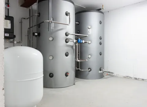 Zwei große Pufferspeicher mit angeschlossenen Rohrleitungen und Messinstrumenten in einem modernen Heizraum. Neben den Speichertanks ist ein weißes Ausdehnungsgefäß sichtbar, das Teil der Heizungsinstallation ist.