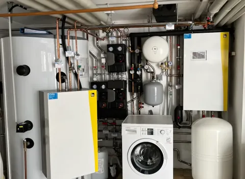 Moderne Heizungsanlage im Technikraum mit großem Pufferspeicher, Hydraulikstation und integriertem Warmwassersystem. Die sauber verlegten Rohrleitungen und Komponenten sorgen für eine effiziente und nachhaltige Wärmeversorgung des Gebäudes.