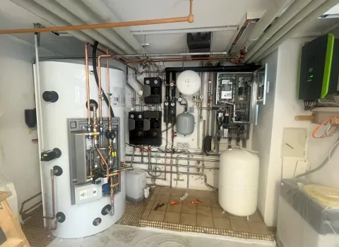 Professionell installierte Heiztechnik mit Pufferspeicher, Ausdehnungsgefäß und intelligenter Regelungseinheit in einem Kellerraum. Die Anlage unterstützt eine nachhaltige Wärme- und Warmwasserversorgung für ein energieeffizientes Wohngebäude.