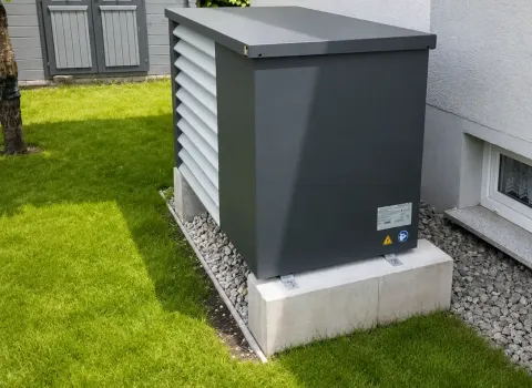 Luft-Wasser-Wärmepumpe mit Schallschutzgehäuse auf einem stabilen Betonfundament neben der Hausfassade. Die kompakte Außeneinheit ist platzsparend installiert und fügt sich harmonisch in den Gartenbereich ein.