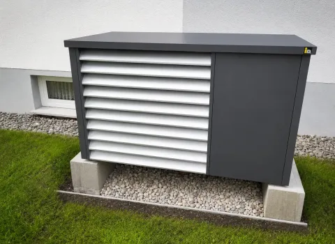 Luft-Wasser-Wärmepumpe mit modernem Schalldämmgehäuse auf einem Betonfundament neben der Hausfassade. Die Lamellenverkleidung reduziert Betriebsgeräusche und sorgt für eine unauffällige Integration in den Gartenbereich.