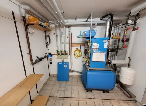 Moderne Heizungsinstallation mit blauem Ölkessel, Ausdehnungsgefäß und verzweigtem Rohrsystem in einem Kellerraum. Die Anlage dient der zuverlässigen Wärme- und Warmwasserversorgung eines Wohngebäudes.
