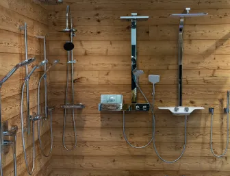 Ausstellungsfläche der Stübler GmbH mit einer breiten Auswahl an Duschsystemen vor einer Holzverkleidung, darunter Regenduschen, Handbrausen und Duschsäulen in verschiedenen Designs.