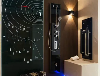 Design-Duschkabine im Showroom der Stübler GmbH mit schwarzer Duschsäule, stilvollem Sitzbereich, indirekter LED-Beleuchtung und künstlerisch bedruckter Glaswand mit Wettergrafik.