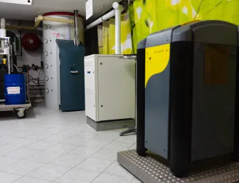 Technikraum der Stübler GmbH mit verschiedenen Heiz- und Speichersystemen, darunter Solvis-Module und eine Pellets-Heizung vor grün bedruckter Wand.