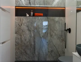 Modernes Duschbad der Stübler GmbH mit großflächiger Marmoroptik, Regendusche, schwarzem Duscharmatur-Set und hinterleuchtetem Ablagefach mit roten Akzenten.