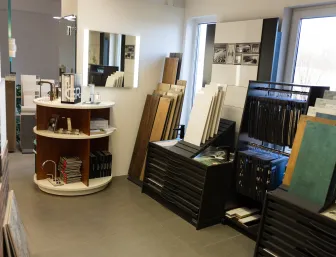 Material- und Armaturen-Ausstellung der Stübler GmbH mit Fliesenmustern, Holzbodenbeispielen, Waschtischarmaturen und Katalogen in einem hellen Showroombereich.