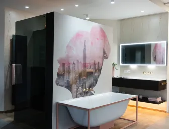 Ein modernes Badezimmer der Stübler GmbH mit freistehender Badewanne vor einer künstlerisch gestalteten Wand sowie einem beleuchteten Spiegel über einem stilvollen Waschbecken.