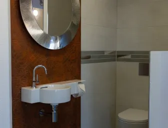 Kompaktes Gästebad in der Ausstellung der Stübler GmbH mit rundem Designer-Spiegel, schmalem Waschbecken und WC in neutralen Beige- und Brauntönen.