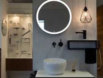 Stilvoll inszenierter Waschplatz der Stübler GmbH mit rundem, beleuchtetem Spiegel, schwarzer Aufsatzarmatur und moderner Pendelleuchte im geometrischen Design.