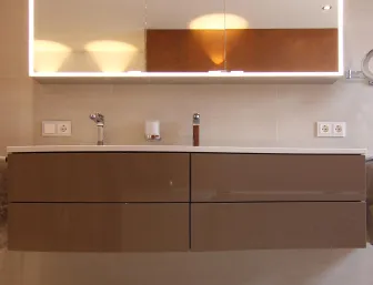 Moderner Doppelwaschtisch mit Hochglanz-Fronten, beleuchtetem Spiegelschrank und seitlichen Handtüchern in einem eleganten Badezimmer.