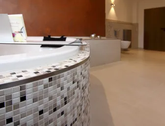 Detailaufnahme der Mosaikfliesen einer modernen Eckbadewanne in einem stilvollen Badezimmer mit warmen Wandfarben.