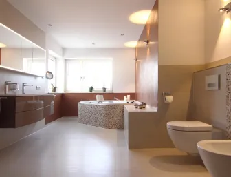 Großzügiges Badezimmer mit beleuchtetem Spiegelschrank, Doppelwaschtisch, Eckbadewanne mit Mosaikfliesen, WC und Bidet in modernem Design.