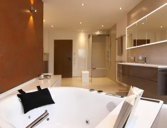 Luxuriöses Badezimmer mit moderner Whirlpool-Badewanne, beleuchtetem Doppelwaschtisch, großer begehbarer Dusche und warmen Wandakzenten.