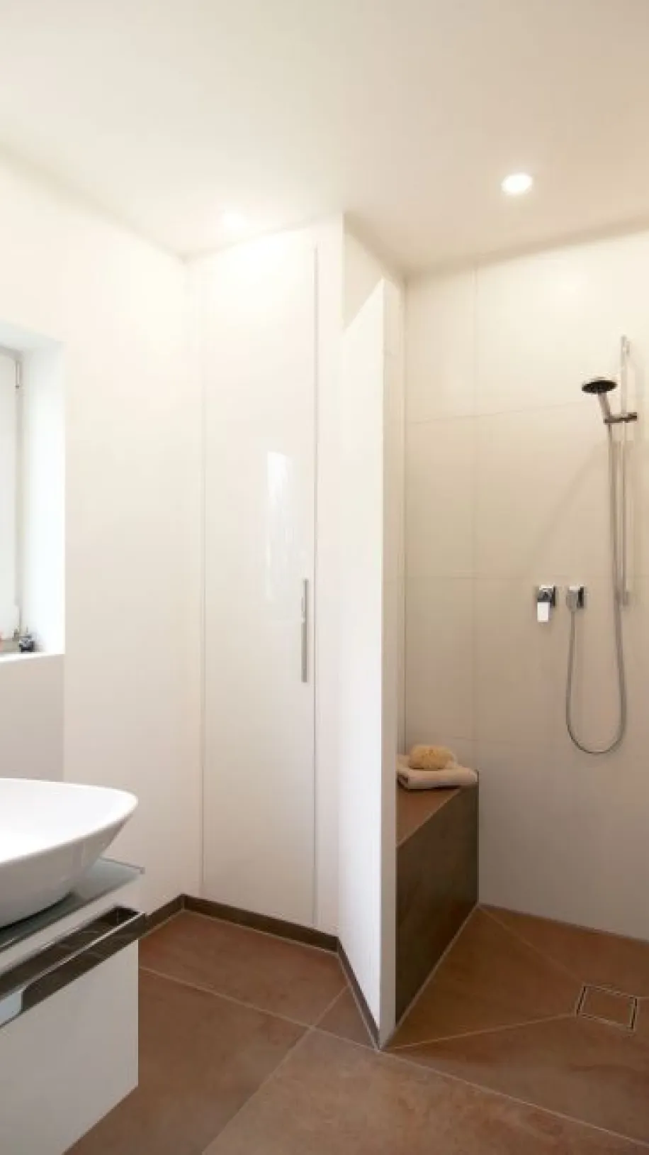 Modernes Gäste-WC mit offener Dusche, bodengleichem Einstieg, weißer Wandgestaltung und braunen Bodenfliesen, ergänzt durch ein elegantes Aufsatzwaschbecken.